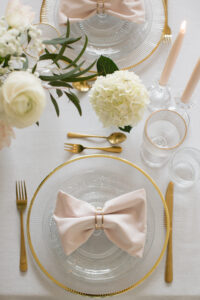 Elegantne laud, kaetud kuldse servaga klaasnõude ja riidest puuderroosade servjettidega — Just See renti valmis nõudekomplekt stiilseks ja lihtsaks lauakatteks.